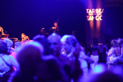 Un violoniste avec des danseurs de tango dans une ambiance violette avec écrit tarbes en tango en lettres lumineuses sur le fond.