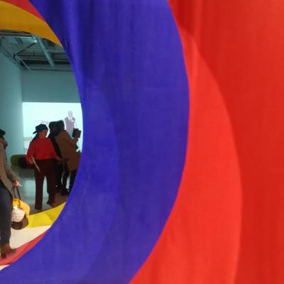 des drapés de couleur rouge et bleu, une vidéo et des visiteurs de l'exposition