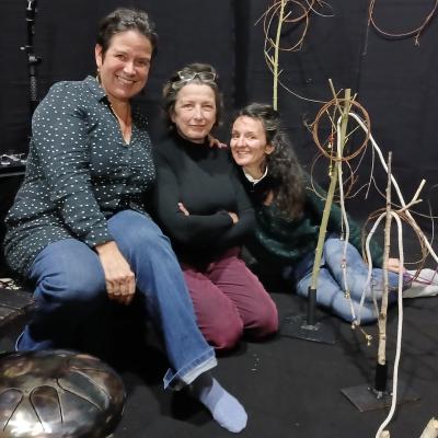 Maya Paquereau au milieu de son spectacle avec 2 autres personnes, elles sont assises par terre dans leur décor fait de noir, de ficelles et de micro et autres instruments de musique.
