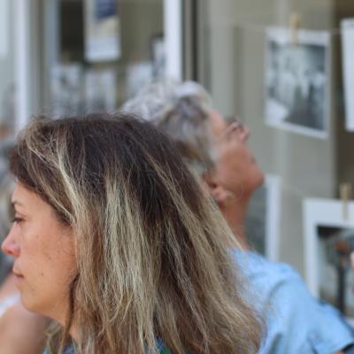 Une femme de profil à l'avant de la photo, et en arrière plan une autre personne regardant des photos exposées sur une vitrine
