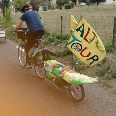 dans la campagne, des vélos avec remorque et dreapeau fait main sur lequel on lit altertour 