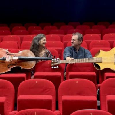 deux musiciens avec guitare bass et violoncelle dans des fauteuils rouges au milieu d'une salle de cinéma
