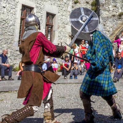 deux combattants habillés en tenue du moyen-âge se battent avec épées et bouclier dans la cour du château