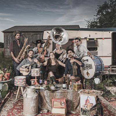 Un groupe genre fanfare devant une caravane et des tenues bigarrées dans un style gitan assumé