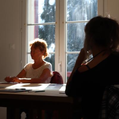 Le soleil traverse la fenêtre pour se poser sur les cheveux d'une femme et une table où sont posés feuilles blanches et crayons