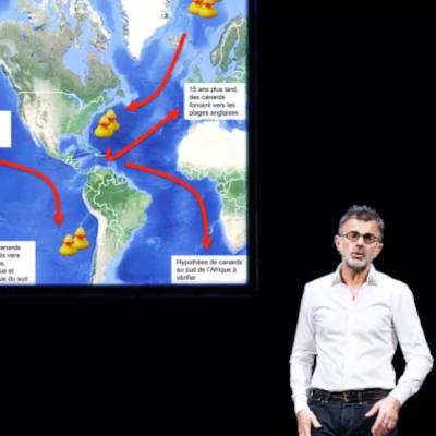un homme en chemise blanche devant un slide de powerpoint avec une carte du monde et un gros canard jaune