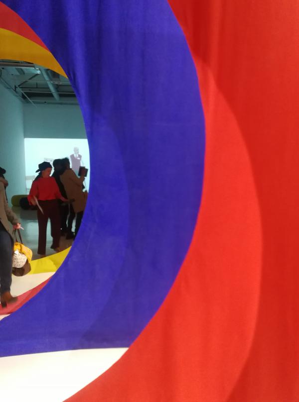 des drapés de couleur rouge et bleu, une vidéo et des visiteurs de l'exposition