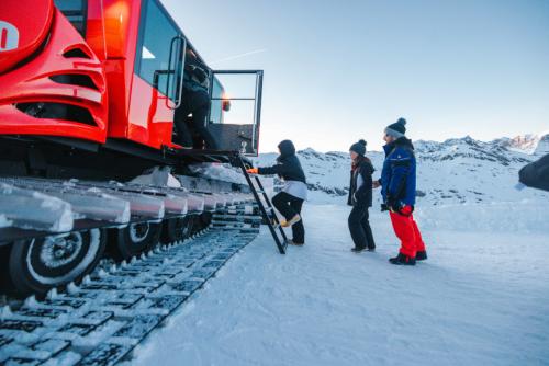 Des touristes montent dans la dameuse sur fond de neige