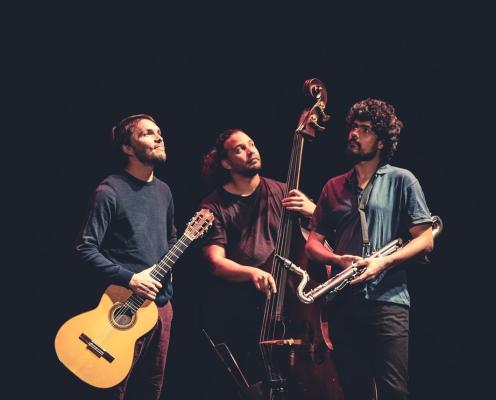 3 musiciens sur fond noir regarde au-dessus d'eux