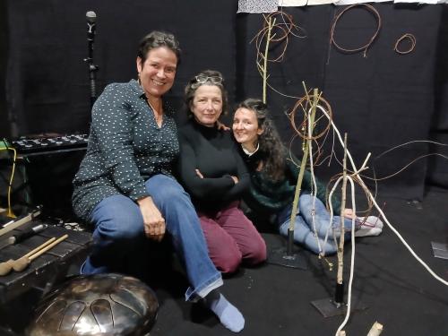 Maya Paquereau au milieu de son spectacle avec 2 autres personnes, elles sont assises par terre dans leur décor fait de noir, de ficelles et de micro et autres instruments de musique.