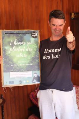 un homme avec un Tshirt où est écrit Homme des bois le pouce levé et un grand sourire. Il tient l'affiche du spectacle