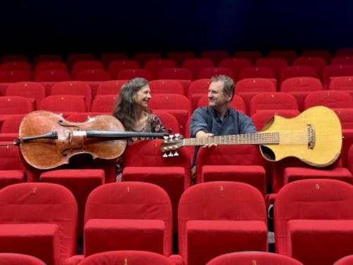 deux musiciens avec guitare bass et violoncelle dans des fauteuils rouges au milieu d'une salle de cinéma