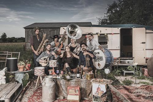 Un groupe genre fanfare devant une caravane et des tenues bigarrées dans un style gitan assumé