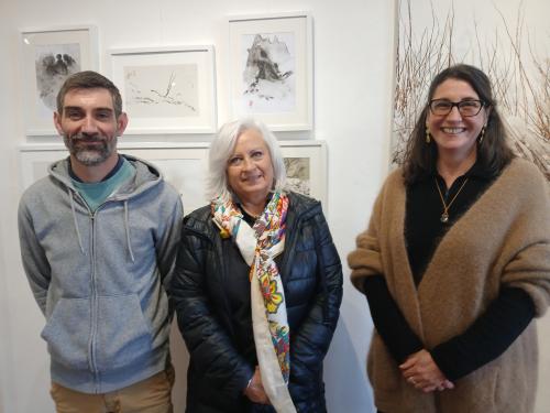 1 homme et 2 femmes souriant devant des tableaux et photographies 